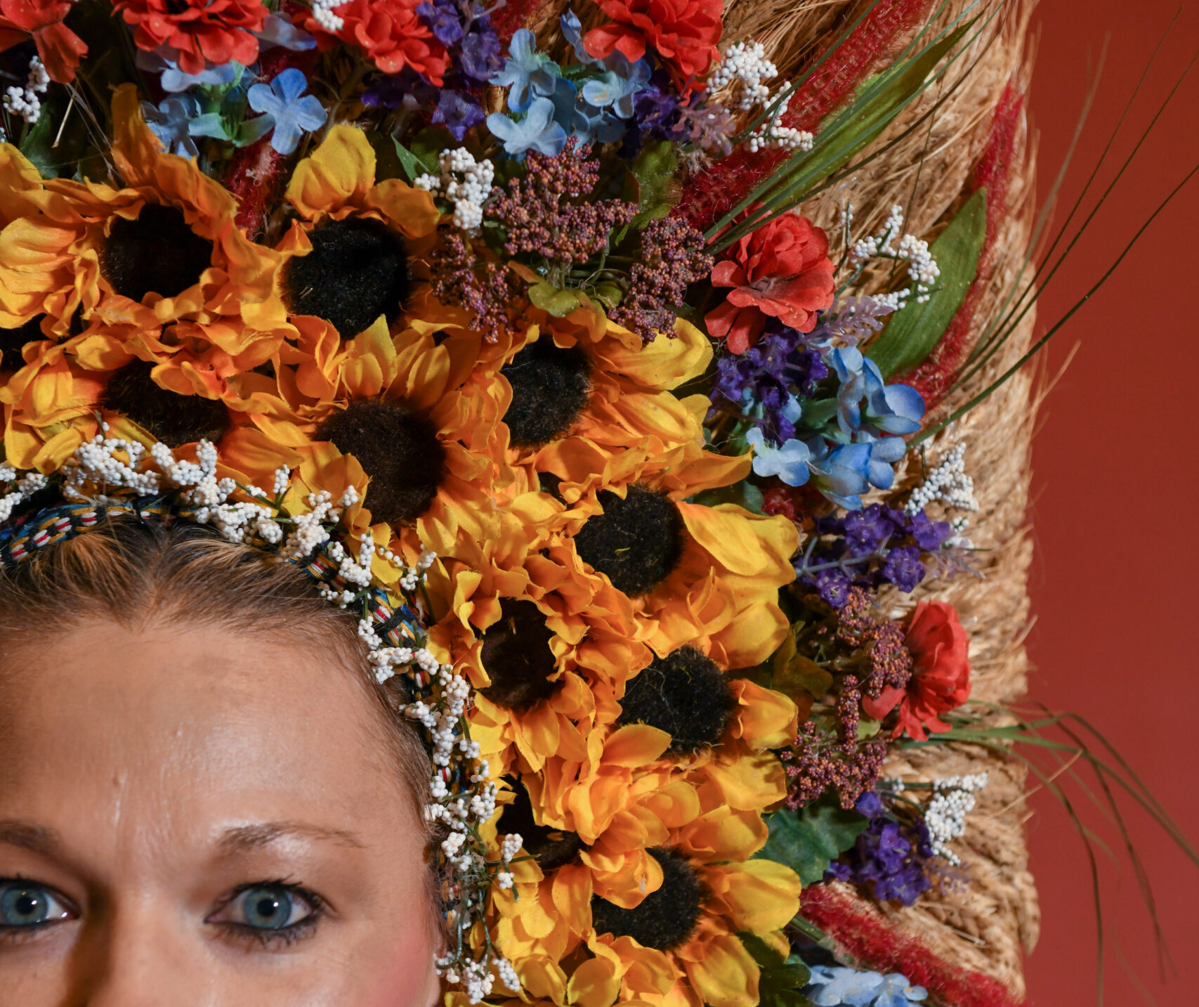 A dancer wears an elaborate headpiece with sunflowers, red and blue flowers, and shoots of wheat.