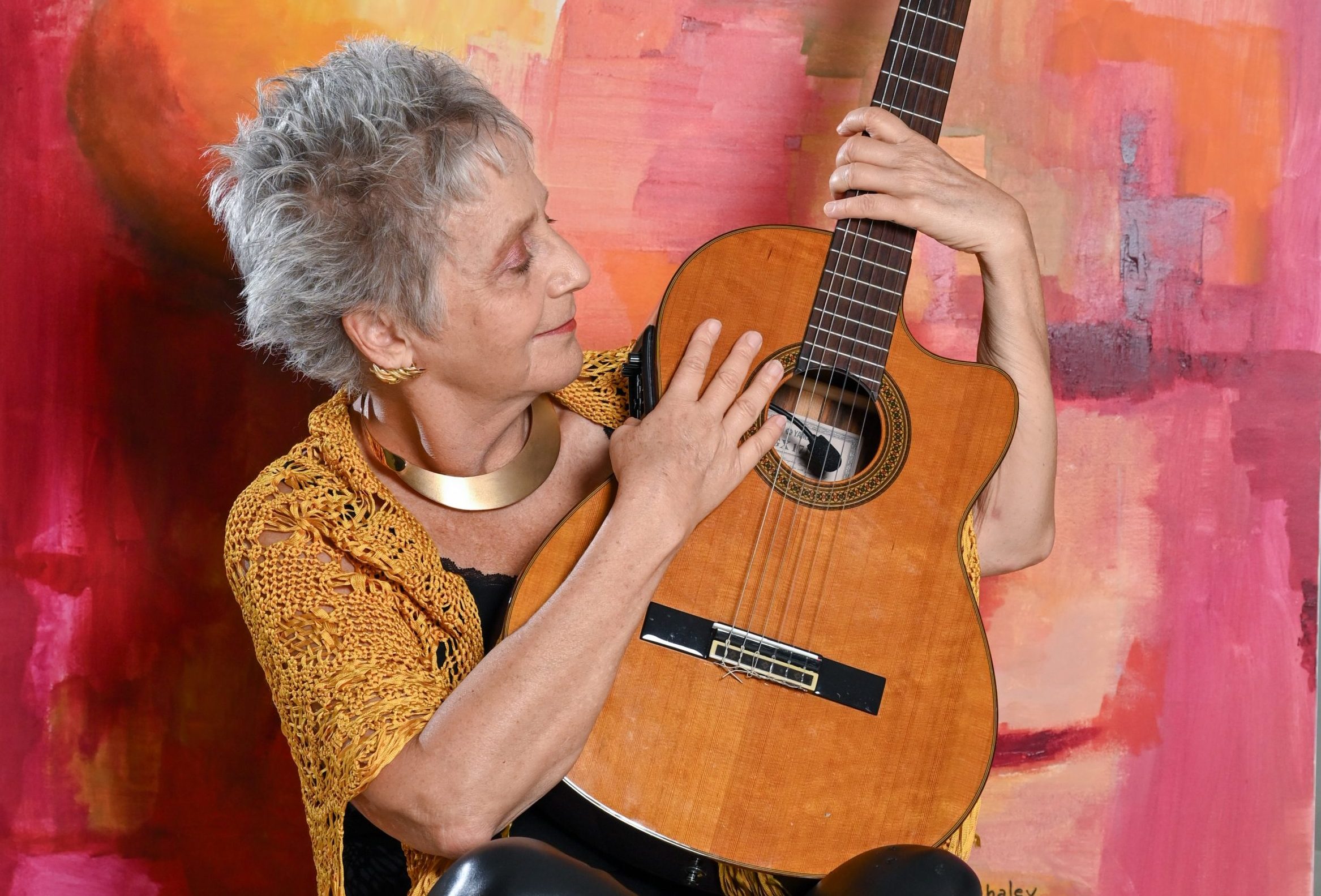 A woman (Alejandra Czarny) holding a guitar in front of her. She is holding the body and neck of the guitar as she smiles and looks at it