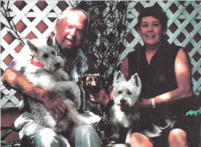 A man and woman, Fred and Gerry Smith, sit in their garden, each holding one of their small dogs.