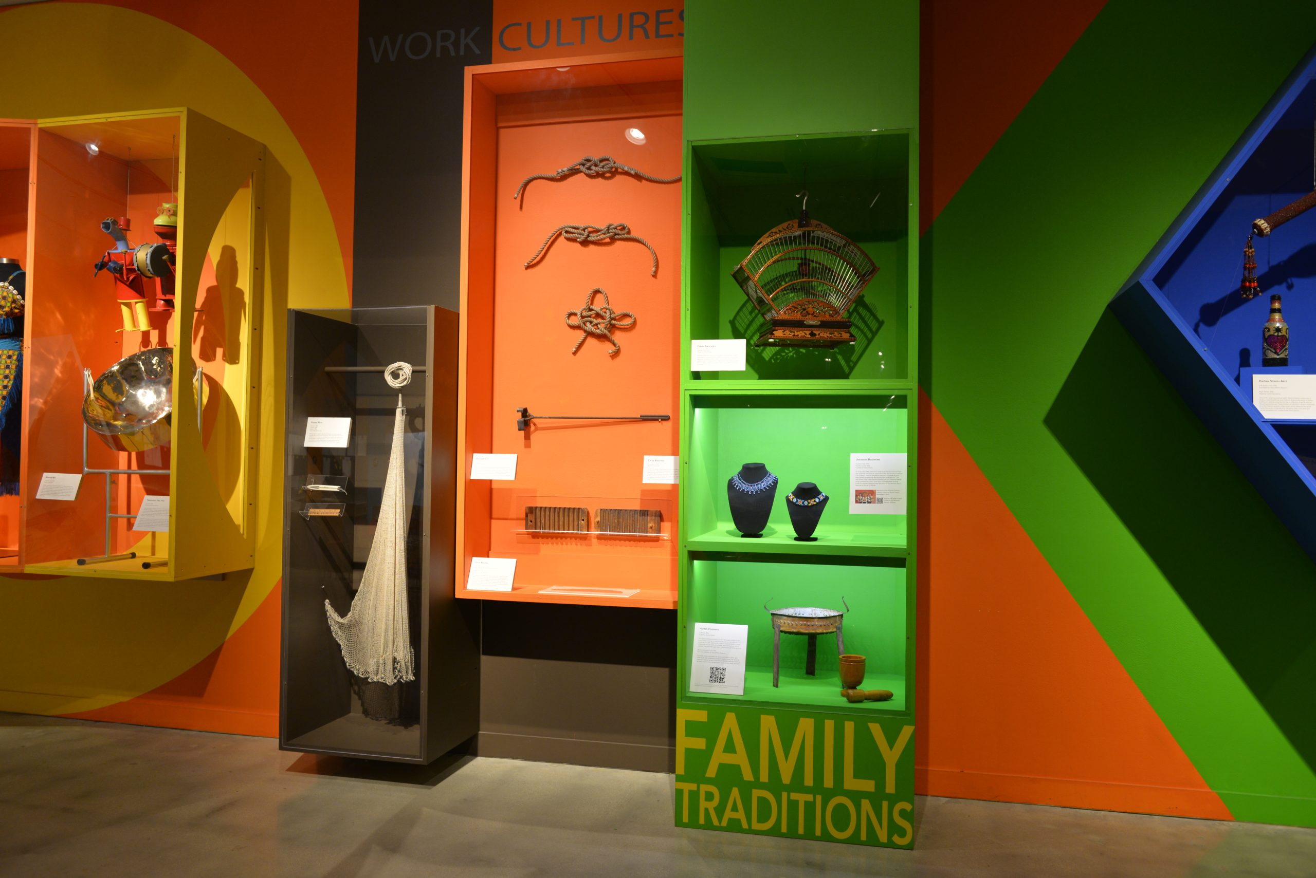 objects encased on the gallery wall include beaded necklaces, a birdcage, a fishing net, and other small items.