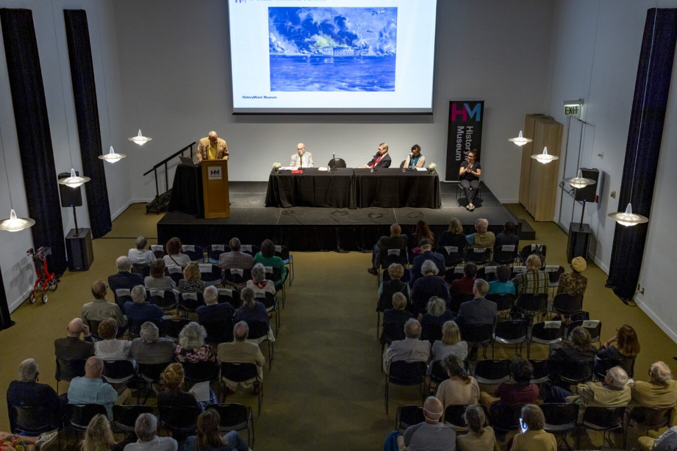 Guest are seated in the museum theatre while looking onward at panelist and their presentation.
