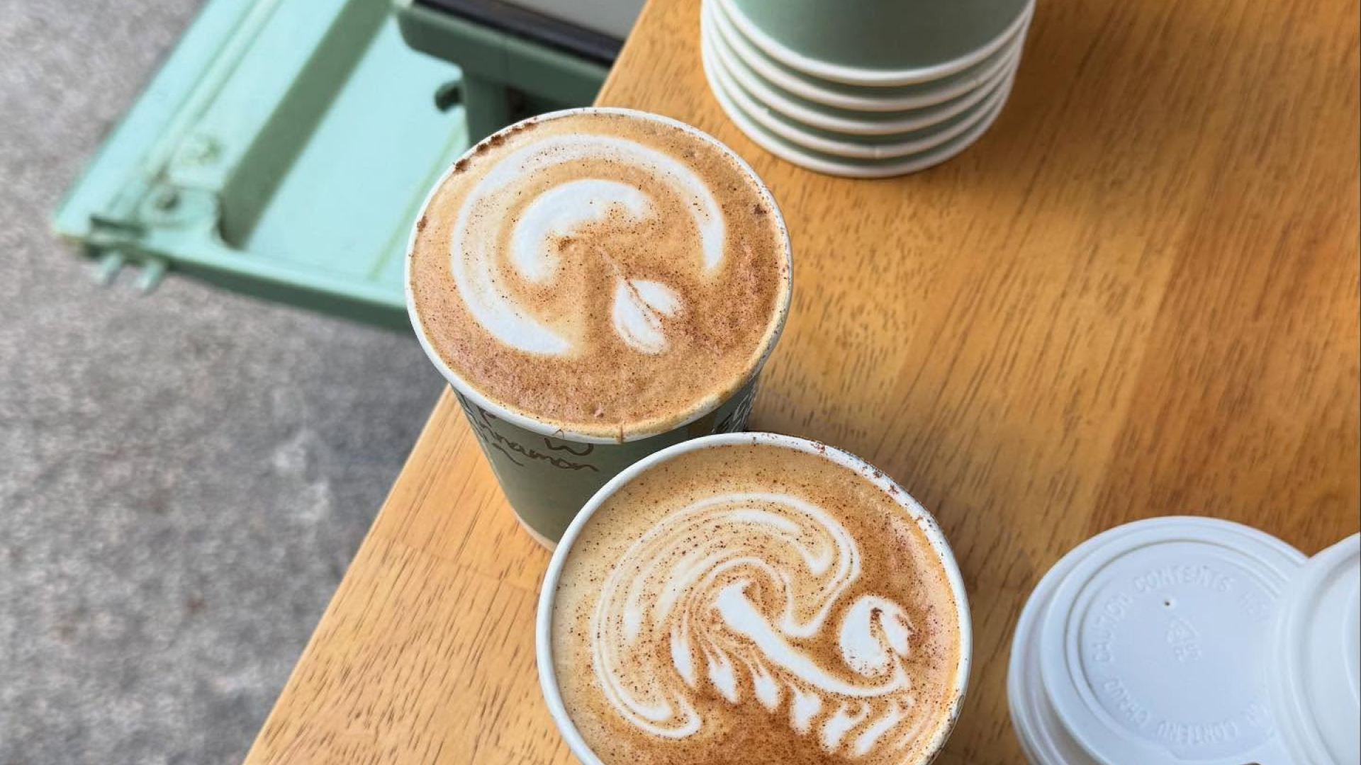 Two lattes with creative foam shapes sit on a wooden table.