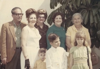 A photo from possibly the 1960s of a group of people. A man and four women stand in the back and three children stand in front of them.