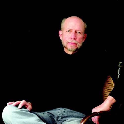 A middle-aged man seated in a chair, looking into the camera.